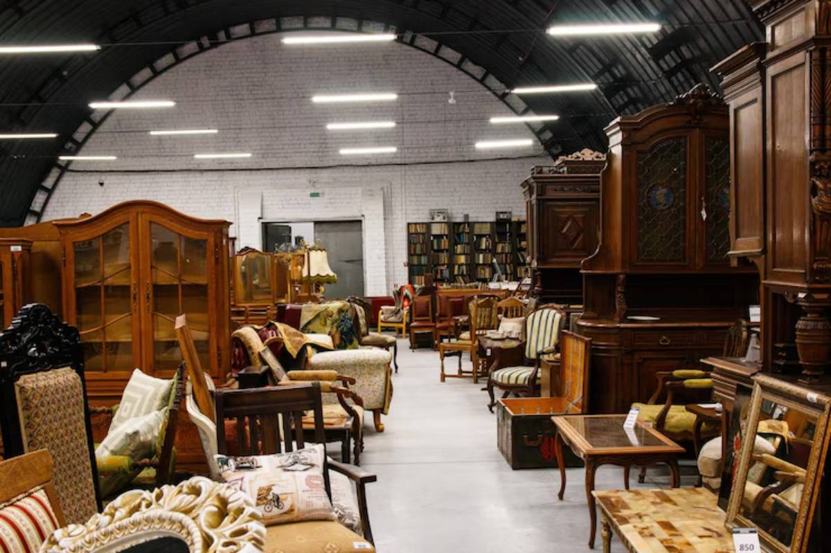 A spacious antique store filled with various wooden furniture pieces, including chairs, cabinets, and tables under bright lighting.