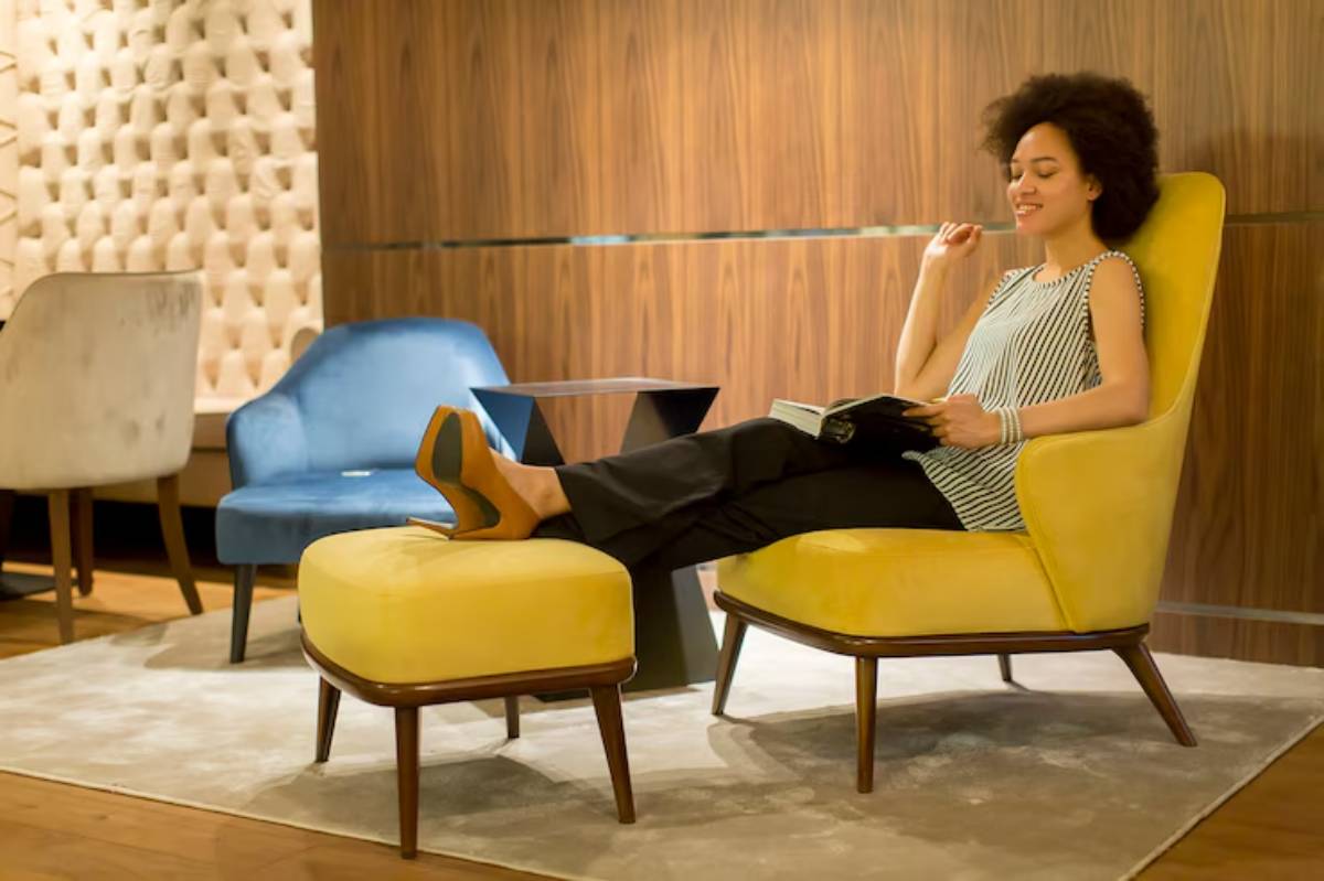 A person relaxes in a bright yellow chair with a matching ottoman while reading a book in a modern, stylish interior.