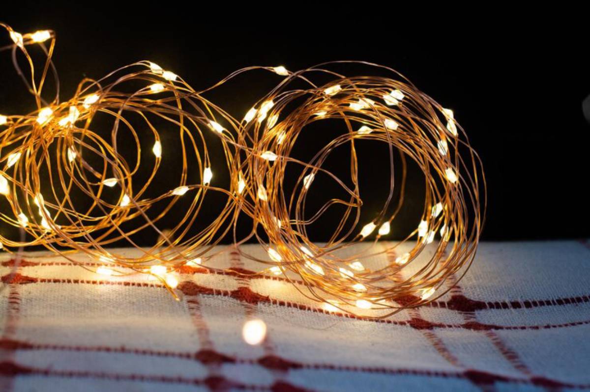 A tangled arrangement of warm white LED fairy lights on a red-checked tablecloth against a black background.