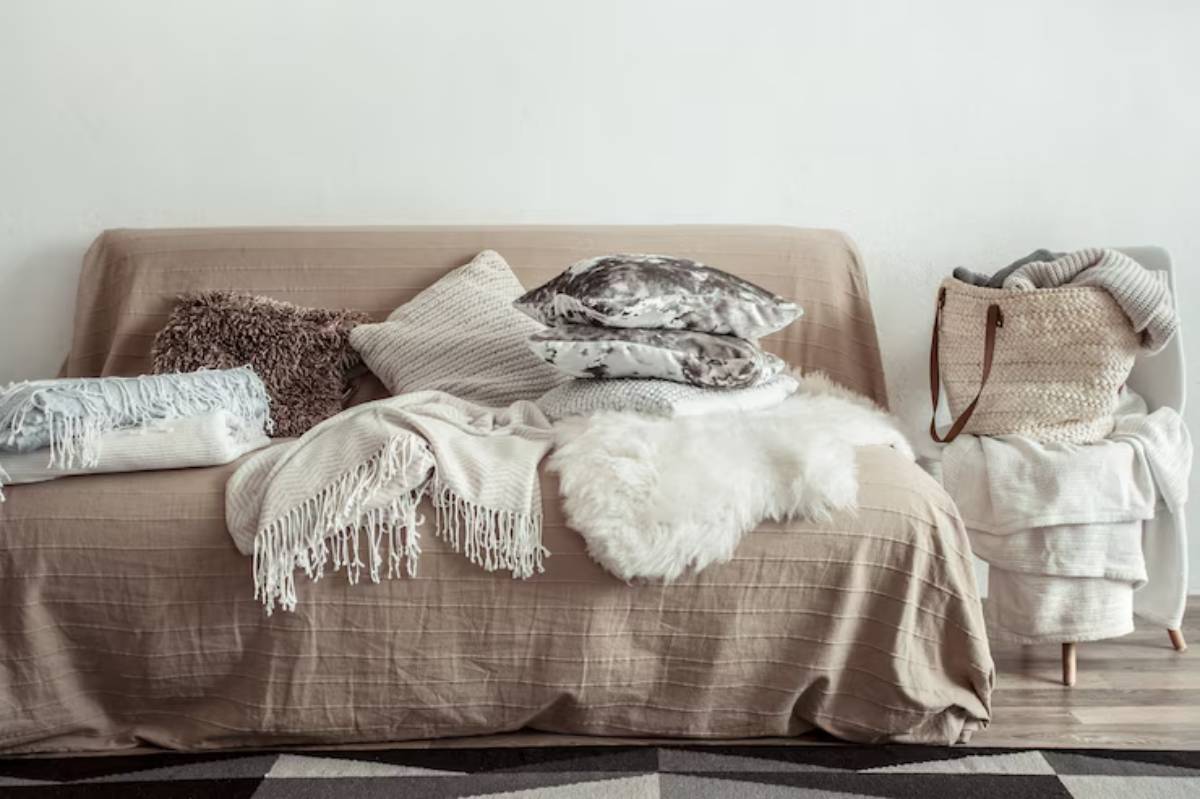 A cozy, neutral-toned sofa adorned with various textured pillows and blankets, complemented by a woven basket of extra throws.