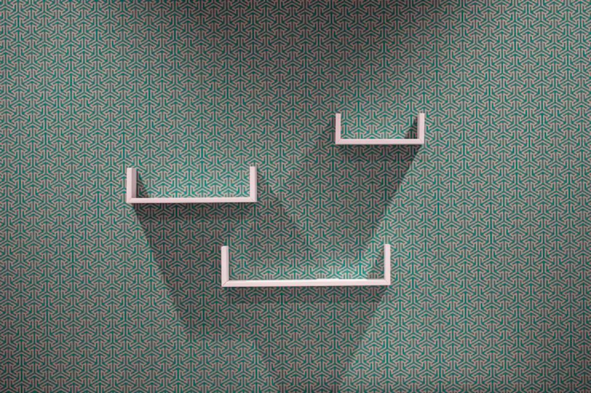 Three minimalist white shelves create geometric shapes against a teal patterned wallpaper, casting subtle shadows.