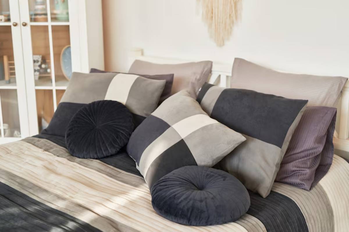 A neatly made bed adorned with a variety of stylish, textured pillows in shades of gray, navy, and cream.