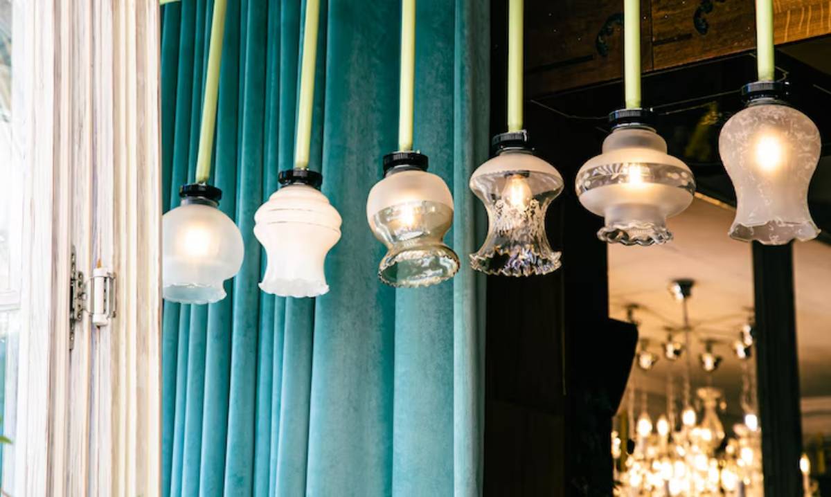 A row of unique pendant lights with various glass shades hangs against a backdrop of teal velvet curtains.
