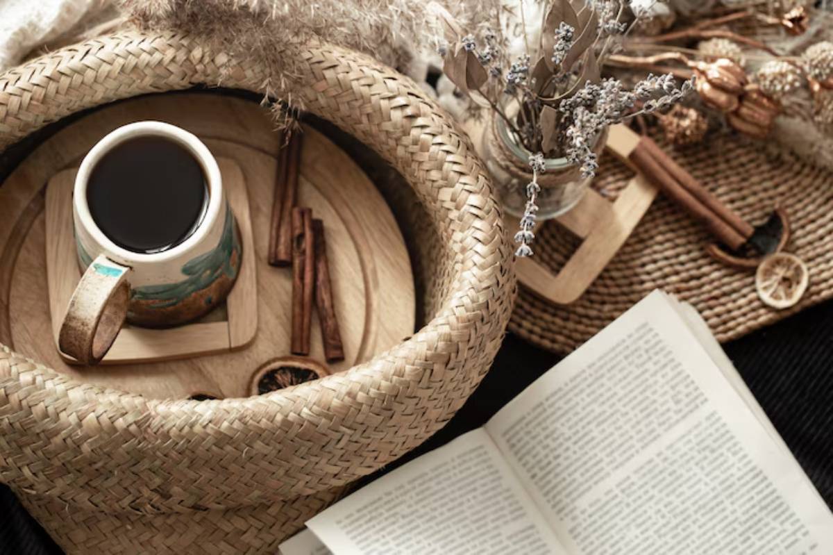 A cozy arrangement with a mug of coffee, cinnamon sticks, dried flowers, and an open book on woven textures.