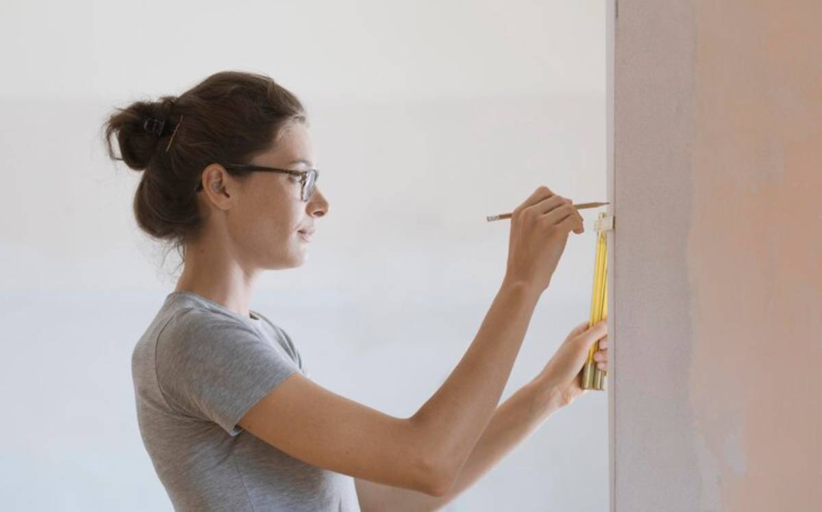 A person stands against a wall, measuring and marking with a pencil, showcasing a focused approach to a home improvement project.