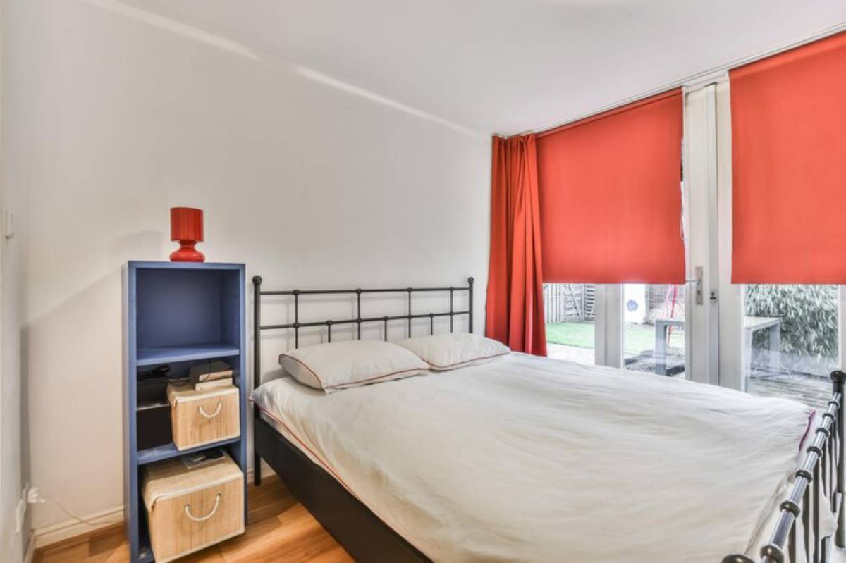 Cozy bedroom featuring a black metal bed, blue shelf with storage boxes, and vibrant orange curtains covering patio doors.