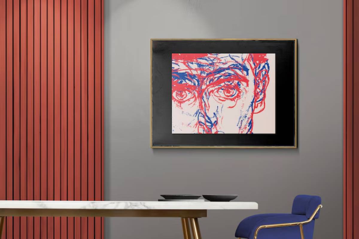 Abstract portrait art in red and blue hangs on a gray wall with a striking red panel, complemented by a modern, minimalist table and chair.