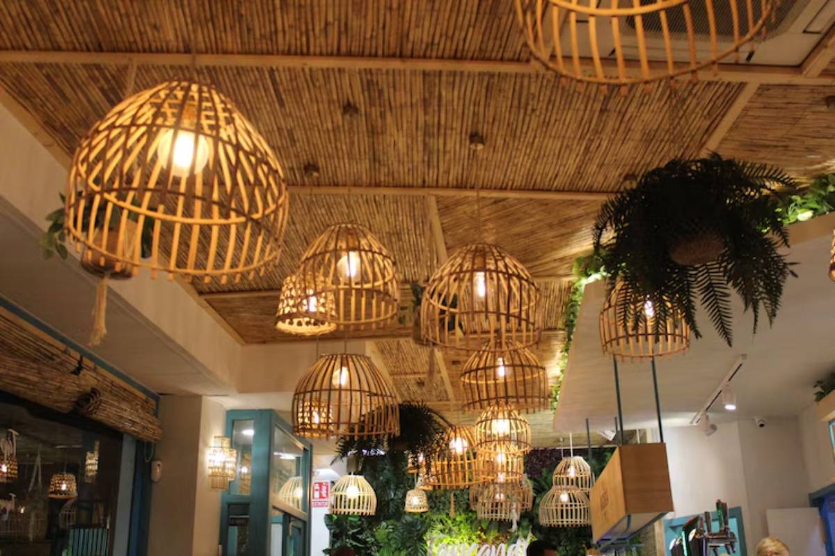 A cozy restaurant interior featuring bamboo pendant lights, lush greenery, and a rustic ceiling, creating a warm, inviting atmosphere.