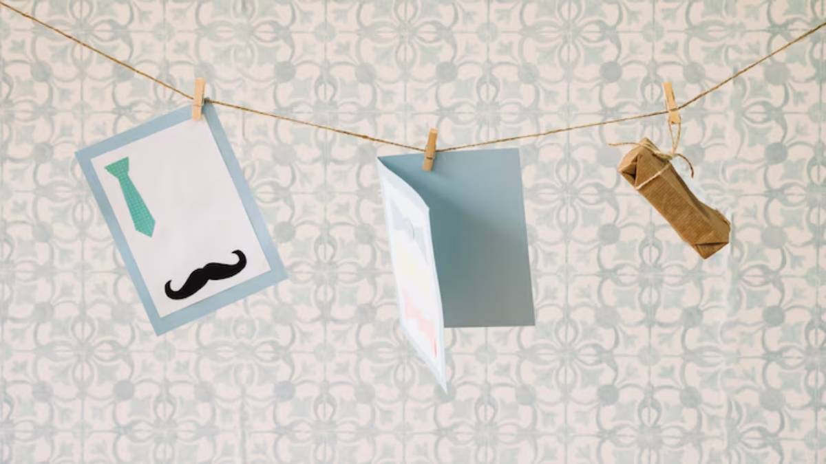 Cards featuring a bowtie and mustache hang from a string against a patterned wall, with a small wrapped gift also displayed.