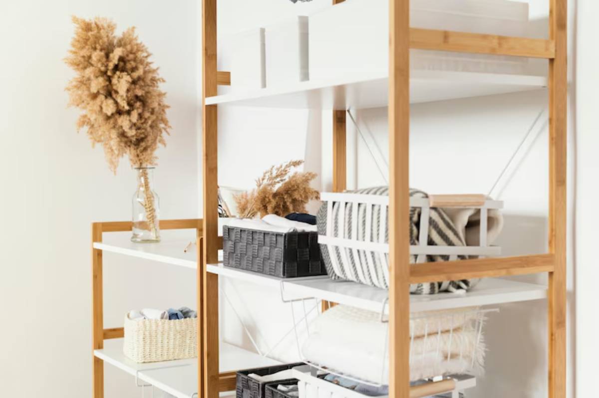 A stylish bamboo shelf with decorative baskets and soft textiles, topped with a vase of dried pampas grass against a white wall.
