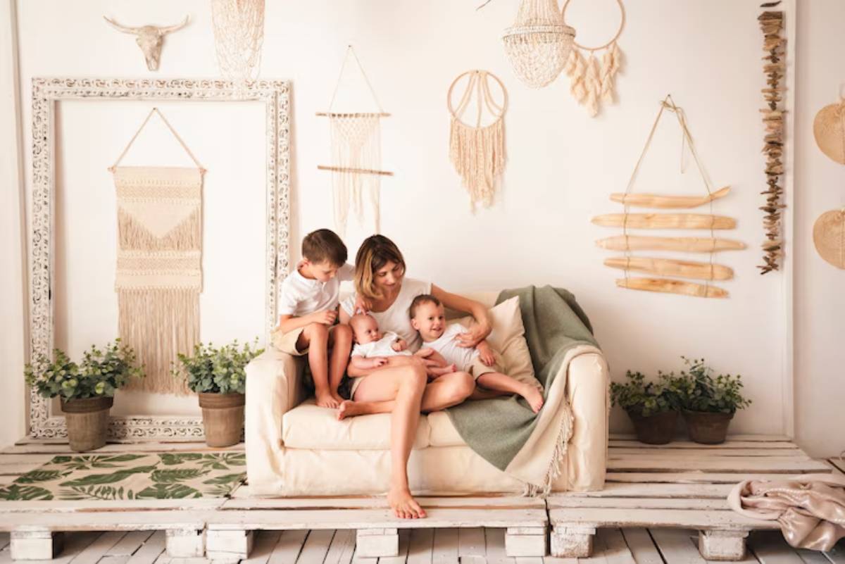 A mother sits on a cozy sofa, surrounded by her three young children, in a beautifully decorated room with bohemian décor.