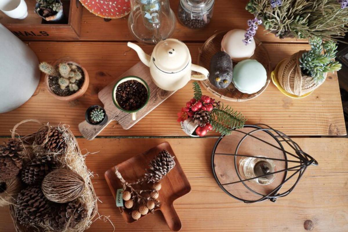 An overhead view of a rustic tabletop featuring coffee beans, succulents, pinecones, a teapot, and decorative macarons.