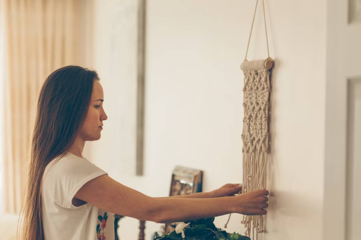 A person installs a macramé wall hanging, surrounded by soft natural light and a soothing indoor setting.