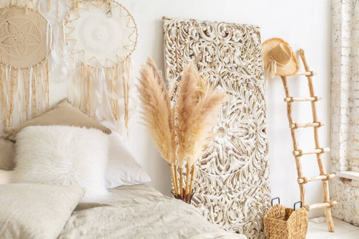A cozy bedroom featuring a plush bed with neutral linens, decorative wall hangings, pampas grass, and a wooden ladder.