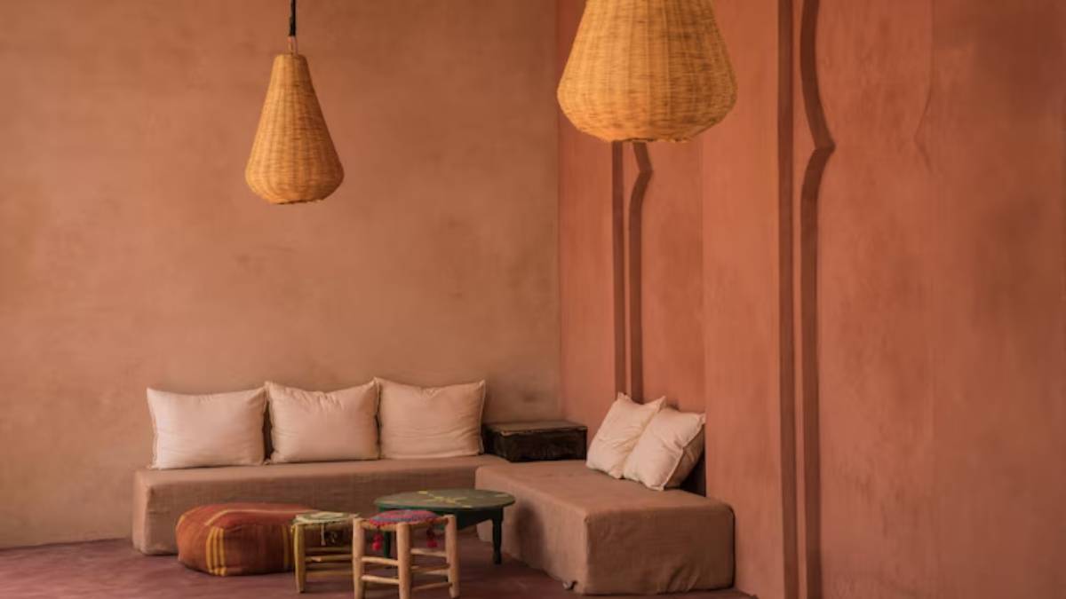 Cozy seating area with beige cushions, a patterned pouf, and woven pendant lights against a warm, earthy wall.
